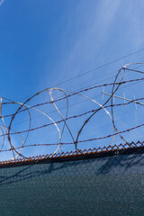 Rolls of barbed wire and razor wire on top of a chain link fence with a deep blue sky background