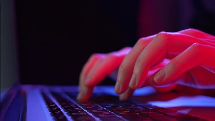 Young woman hands type on keyboard buttons of laptop working distantly at neon purple and pink illumination extreme closeup