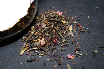 Dry tea with green leaves in spoons, on black background.