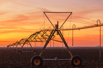Lateral move agricultural irrigation system on plowed field in sunset