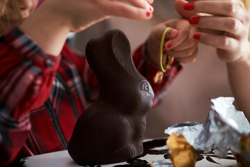 Hands of a woman and a girl opening the wrapping of an Easter chocolate rabbit