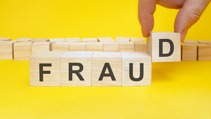 man making word Fraud with wooden cubes at yellow table, closeup. Space for text