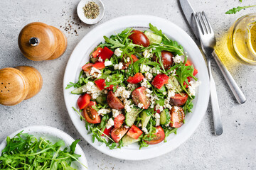 Delicious fresh vegetable salad with arugula, goats cheese and cherry tomatoes on a plate, table top view, concrete background