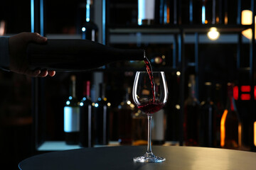 Man pouring red wine from bottle into glass indoors, closeup