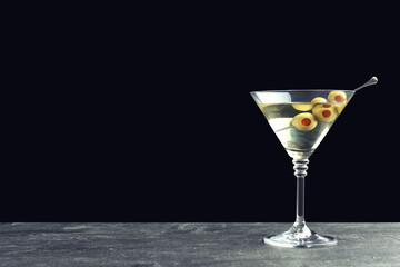 Martini cocktail with olives on grey table against dark background, space for text