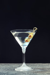 Martini cocktail with olives on grey table against dark background, space for text