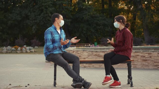 social distance. man and a girl in in protective face mask sitting on bench talking. pandemic coronavirus concept. two masked lifestyle men observe greetings avoid touching. social distance covid 19