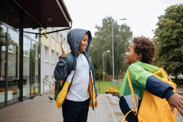 Schoolboys with backpacks. Two African American boys next to the school. Back to the school concept. Kids standing outside and happy to meet each others. Happy black children. First day of school