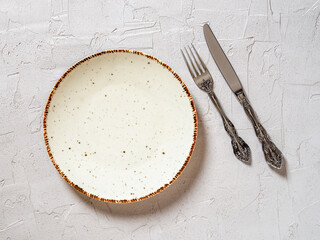 White porcelain dinner plate, vintage table knife and fork on a textured gray background. Empty...