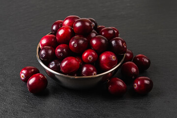 Close-up of red ripe cranberries in a metal bowl on a black slate slab.  Wild berries as superfood, antioxidant and vitamin healthy eating. Ingredient for desserts, Thanksgiving and Christmas dishes.