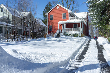 red suburban house and driveway with car tracks cleaned the day after the snow storm