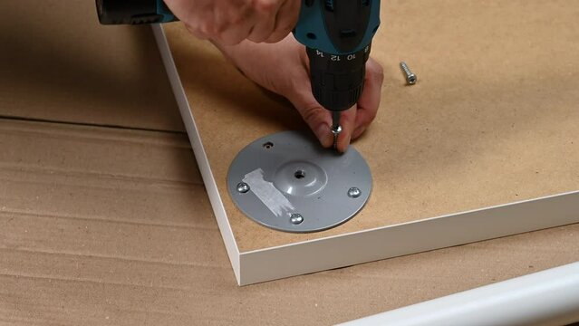female hand screwing a white metal leg into the table cover, self-assembly of furniture