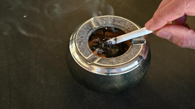closeup of full ashtray and man smoking a cigarette
