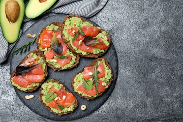 Delicious sandwiches with salmon, avocado and herbs on grey table, flat lay. Space for text