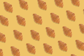 Creative pattern made of freshly baked croissant on bright yellow background.