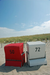 A red and white beach chair with number 50 and 72 on it in front of dunes and dune grass and a blue...