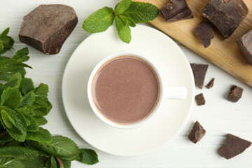 Cup of delicious hot chocolate, chunks and fresh mint on white wooden table, flat lay