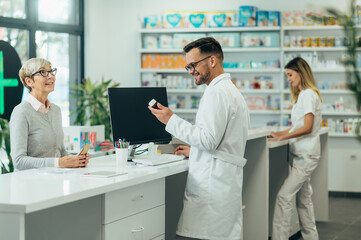 Fototapeta premium Young male pharmacist giving prescription medications to senior female customer in a pharmacy