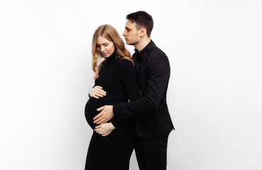 man stands behind his pregnant wife and smiles, hugging her on a white isolated background
