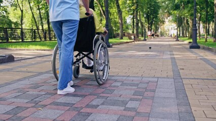 Young woman pushing wheelchair with elderly mother in park, family caregiving - Powered by Adobe