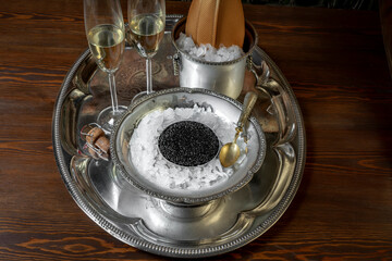 CHAMPAGNE AND BELUGA CAVIAR TIN CAN ON CRUSHED ICE AND SILVER TRAY. LUXURY ROOM SERVICE IN HOTELS.