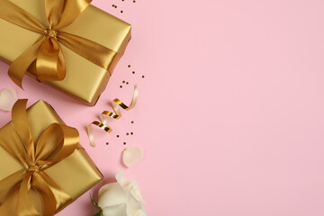 Two golden gift boxes, white rose, confetti and streamer on pink background, flat lay. Space for...
