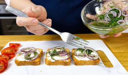 The process of preparing a festive snack on toast with sprats, onions, eggs and tomatoes. close up