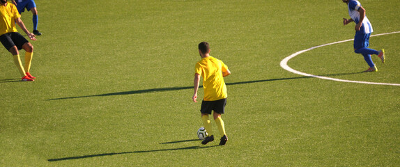Fototapeta na wymiar Momento de um jogo de futebol com disputa de bola na zona do meio campo - equipamentos de cores amarelo, preto, azul e branco