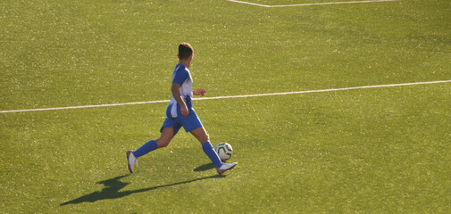 Jogador de futebol com equipamento azul e branco a correr em velocidade com posse de bola numa...