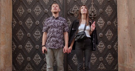 A guy and a girl are standing against the background of old doors. She raises her hand, shows a gesture. Meeting on a date, demonstrating feelings.