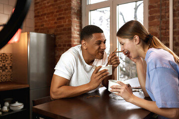 Cheerful multiethnic couple eat noodles for video