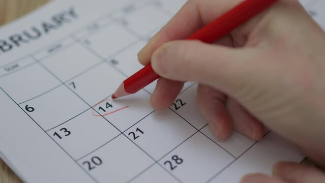 happy Valentine's Day concept: hand writing note shape of heart with red pencil 14 February date month planner paper calendar. celebrating love holiday. note reminding handwritings close-up view