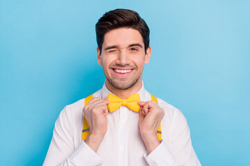 Photo of flirty funky guy dressed white shirt correcting yellow bowtie winking isolated blue color...