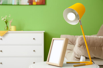 Glowing lamp and blank photo frame on table in room