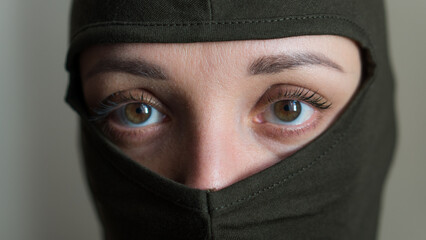 Female portrait of young girl wearing khaki balaclava, only eyes are visible, mandatory conscription, military, feminism, equality concept