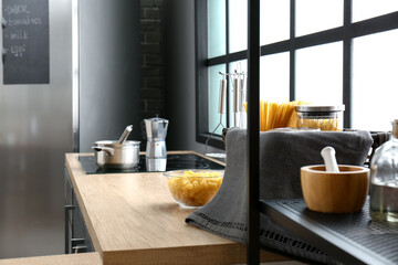 Basket and bowl with different raw pasta and utensils on wooden table top near big window