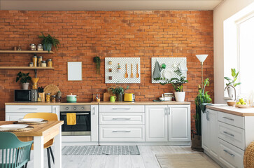 Interior of modern kitchen with white counters, pegboard and brick wall
