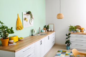 Interior of stylish kitchen with white counters and hanging peg board on green wall