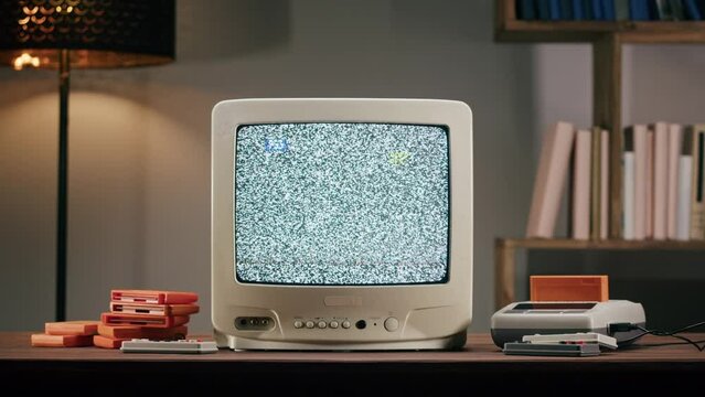 Old television with grey interference screen on home background. Close-up of vintage tv and cartridges for retro playstation. Antique video game, nostalgia. 