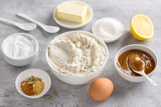 Ingredients for making steamed honey gingerbread: wheat flour, honey, egg, butter, sugar, powdered sugar, lemon, baking powder, spices, on a gray background, top view