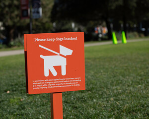 An orange sign requests visitors to keep their dogs on a leash while visiting a park in Los Angeles, CA.
