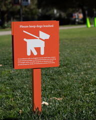 An orange sign requests visitors to keep their dogs on a leash while visiting a park in Los Angeles, CA.