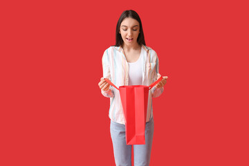Surprised young woman with shopping bag on red background