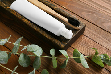 Tube with tooth paste, brush and branch on wooden background