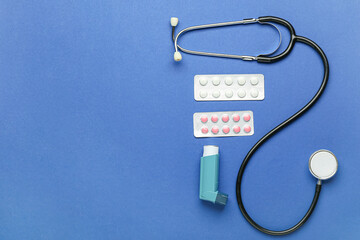 Asthma inhaler, pills and stethoscope on blue background