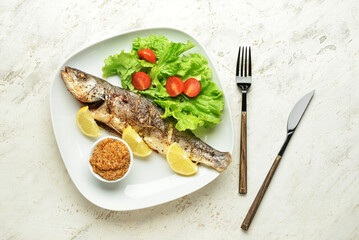 Plate with delicious sea bass fish, vegetables, bowl with mustard seeds and cutlery on light background