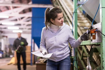 Skilled woman controlling process of olive oil pressing on small factory, looking at gages of equipments