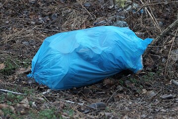 one large ragged blue plastic bag with garbage lies on gray ground in nature