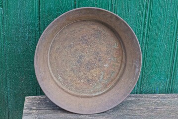 one old brown copper basin stands on a gray wooden table against a green wall