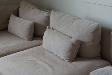 part of a large brown sofa with pillows stands against a gray wall in the room